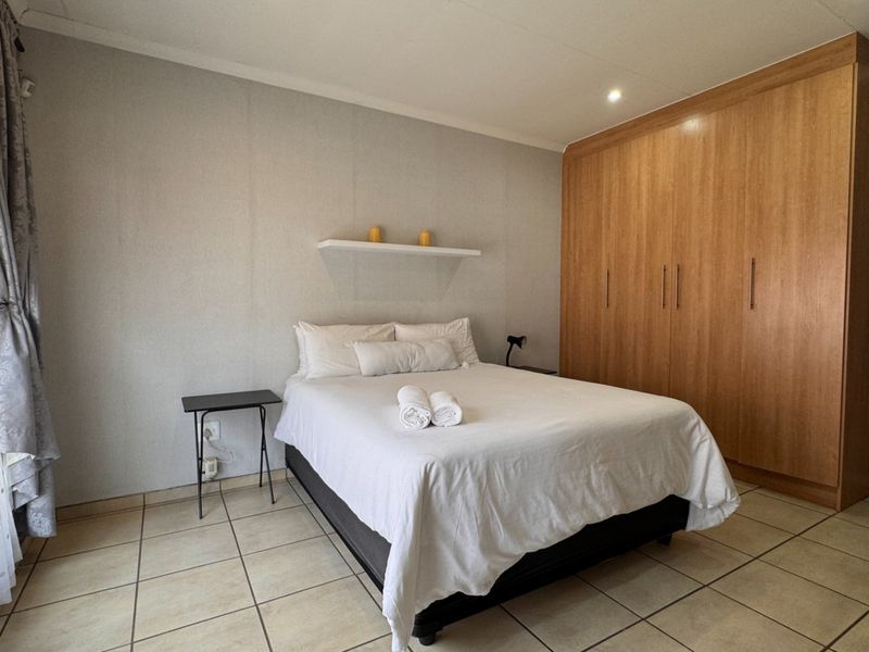 A functional bedroom featuring tiled flooring, a large built-in wooden wardrobe, and a floating wall shelf.