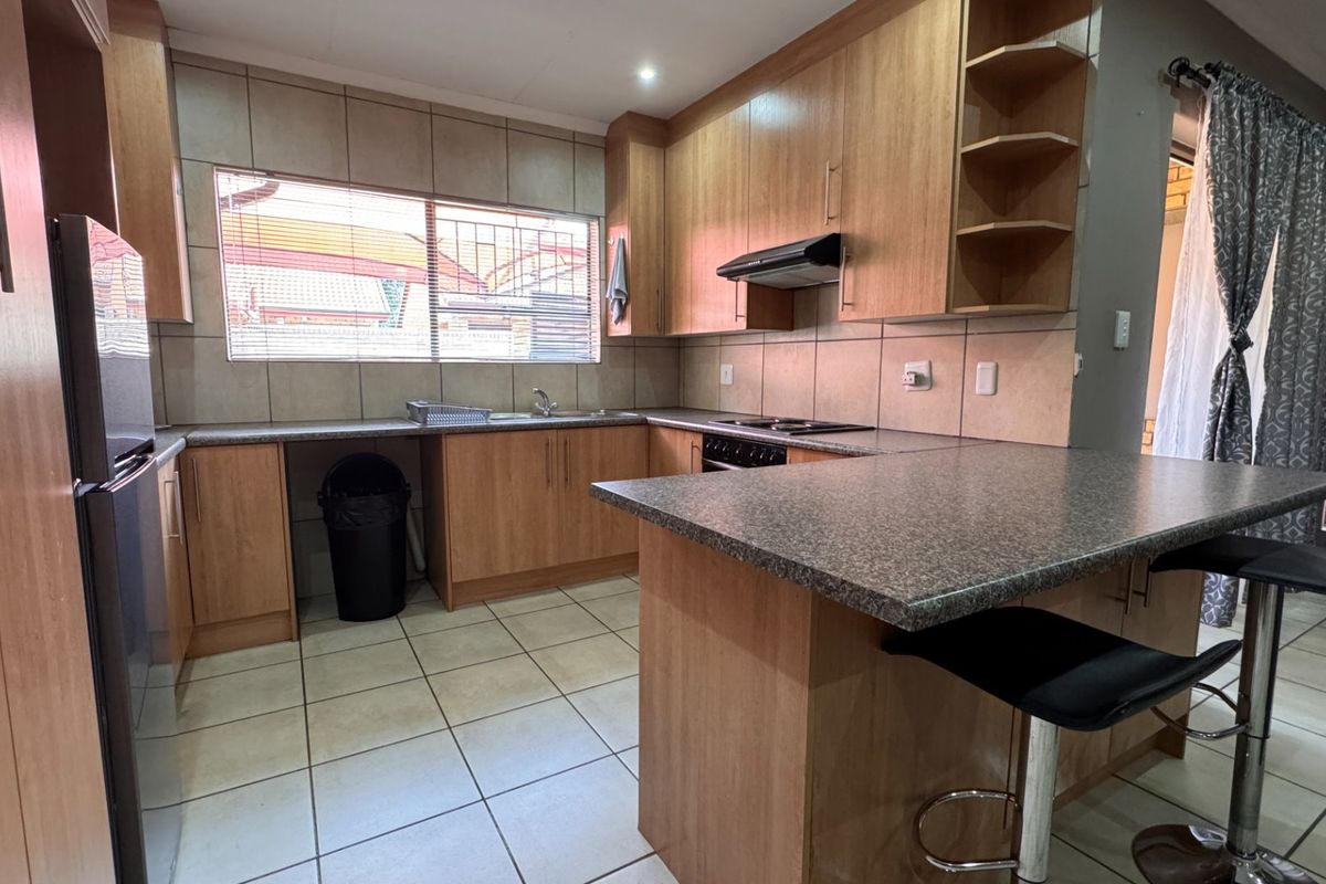 Functional kitchen featuring laminate cabinetry, granite countertops, a breakfast bar, built-in hob with extractor fan, and tiled flooring throughout.