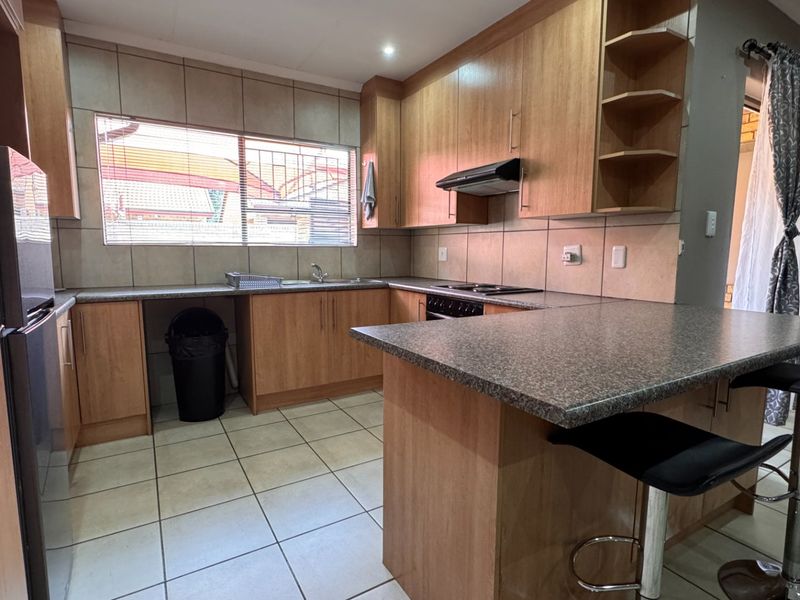 Functional kitchen featuring laminate cabinetry, granite countertops, a breakfast bar, built-in hob with extractor fan, and tiled flooring throughout.