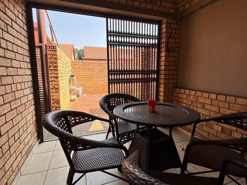 A covered patio area featuring exposed brick walls, tiled flooring, and a security gate leading to an outdoor courtyard space.