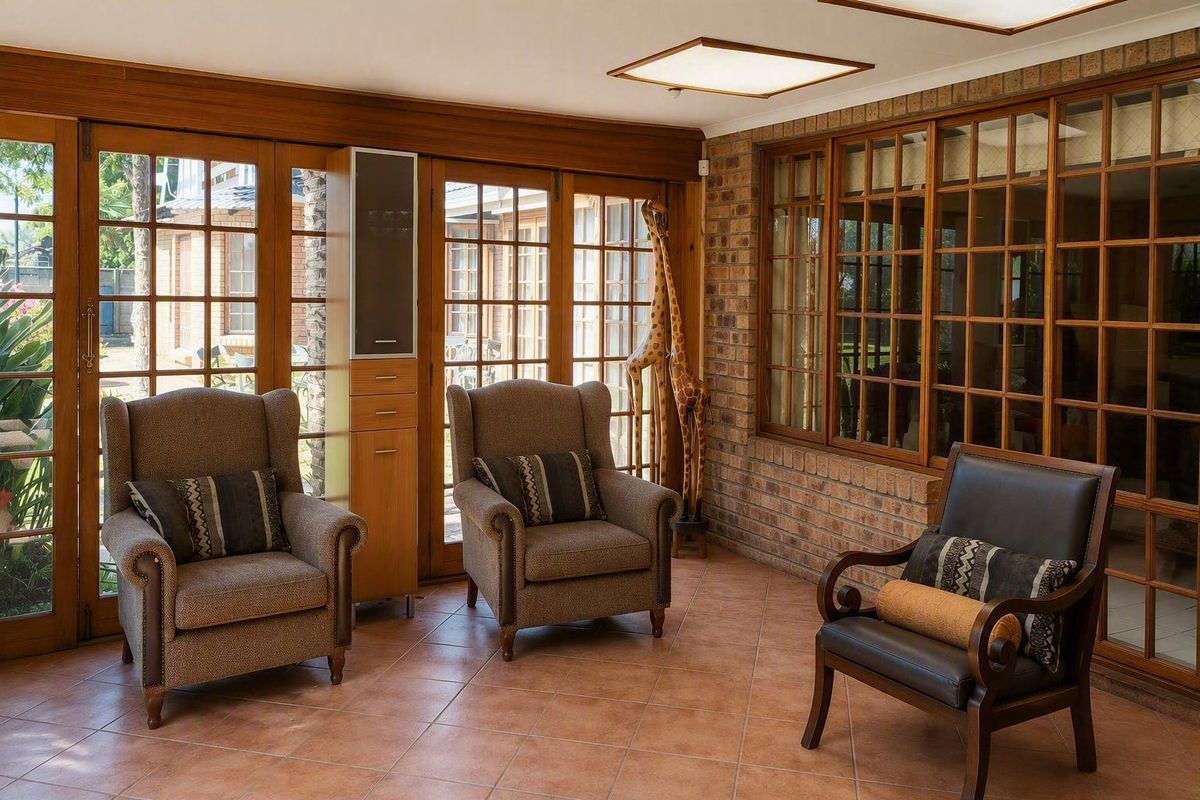 A sun-filled living area featuring exposed brick walls, classic timber-framed glass doors, and large windows that provide ample natural light and garden views.