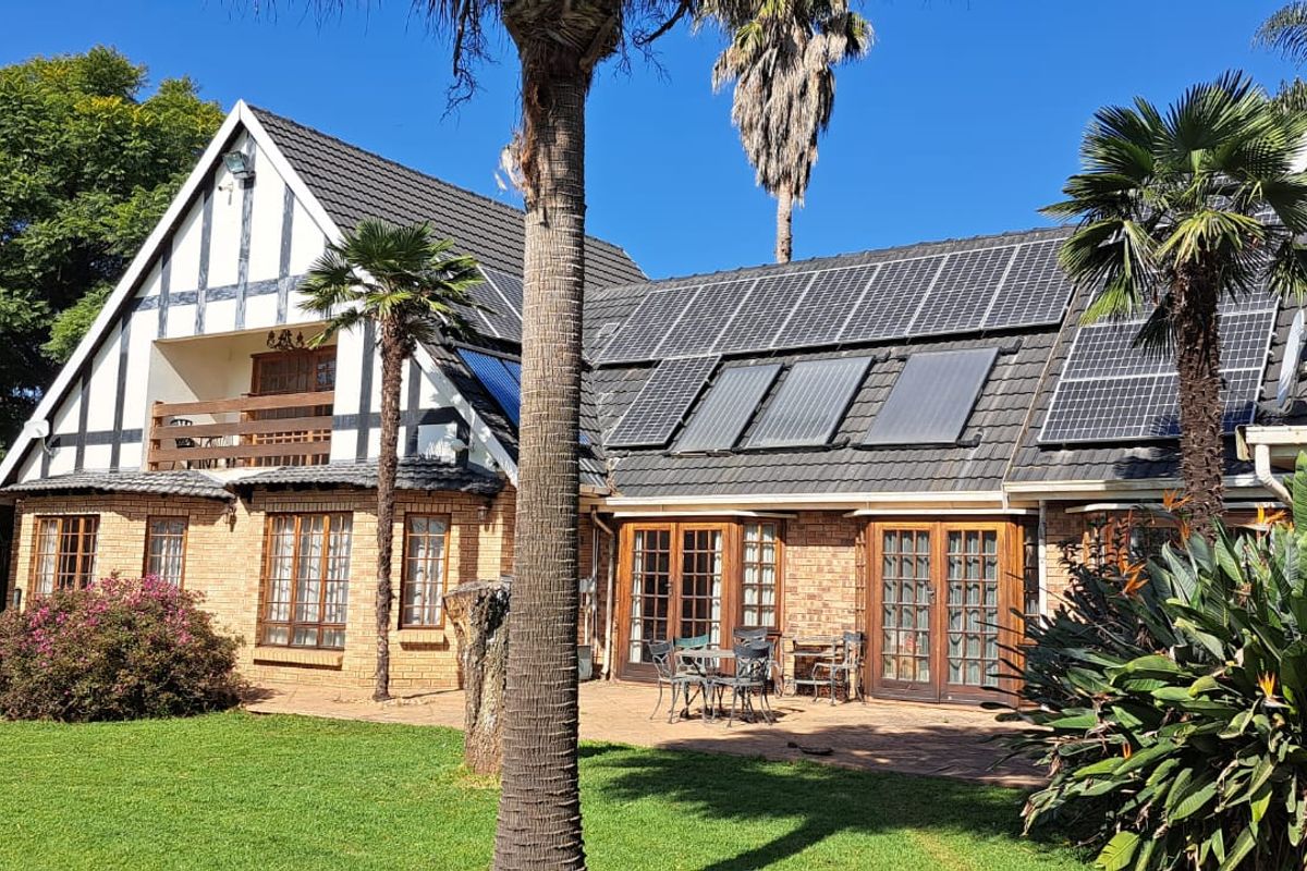 Rear view of a Tudor-style farmhouse featuring a paved patio, balcony, and extensive roof-mounted solar energy and water heating systems.