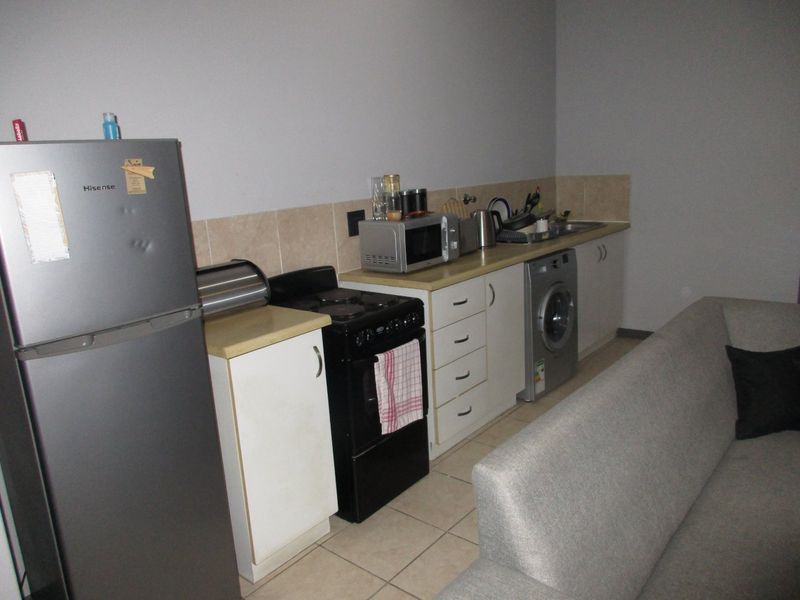 Compact open-plan kitchen area featuring built-in cabinetry, laminate countertops, tiled backsplash, and integrated laundry and cooking appliances.