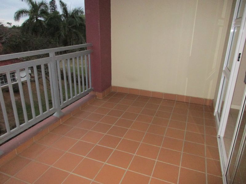 A covered balcony featuring terracotta-style floor tiles, a metal safety railing, and access via a sliding glass door.