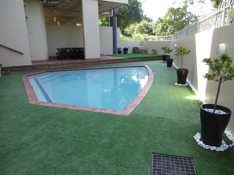 A well-maintained outdoor pool area featuring artificial turf, brick coping, and a clean, paved surround with integrated drainage and perimeter walling.