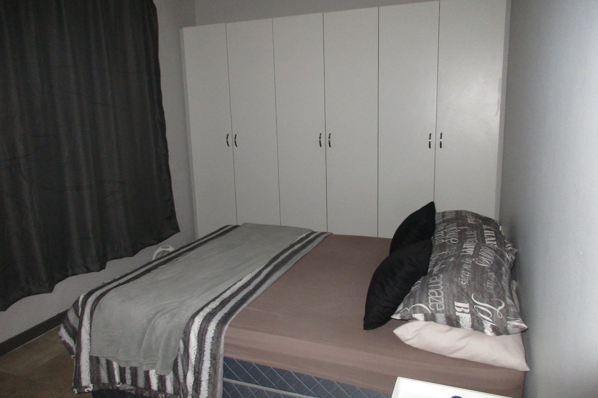 A bedroom featuring neutral wall tones and a large set of white built-in cupboards providing ample storage space.