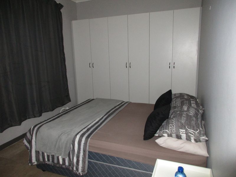 A bedroom featuring neutral wall tones and a large set of white built-in cupboards providing ample storage space.