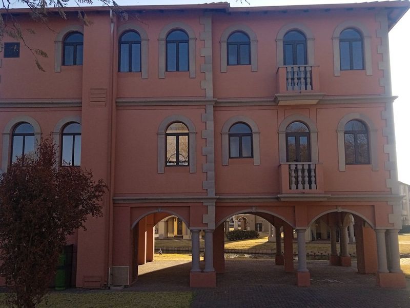 A three-story residential building facade featuring arched windows, balconies, and a ground-level open arcade supported by stone columns.