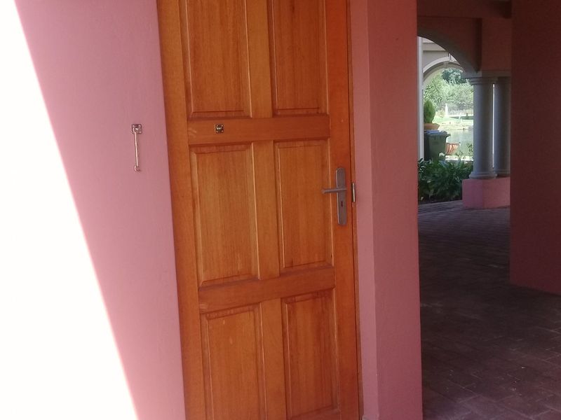 A covered patio area featuring a wooden door, brick paving, and structural columns with arched openings.