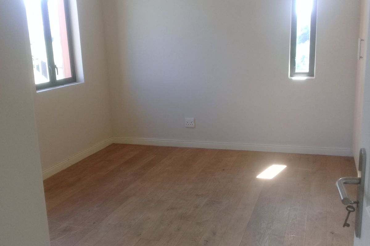 A bright, empty bedroom featuring light timber flooring, neutral walls, and dual windows providing natural light.