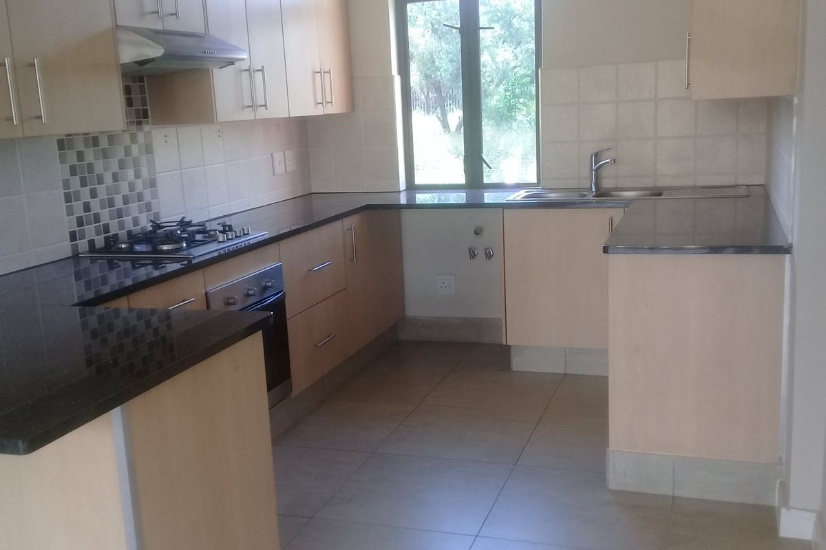 A functional kitchen featuring light wood cabinetry, dark granite countertops, a gas hob, built-in oven, and tiled flooring.