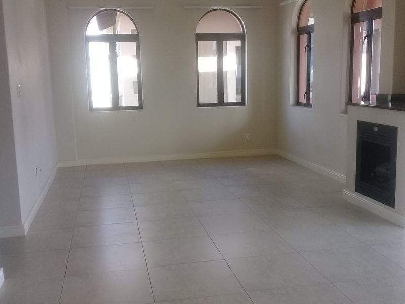Spacious, light-filled living area featuring large arched windows, neutral tiled flooring, and a modern built-in fireplace.