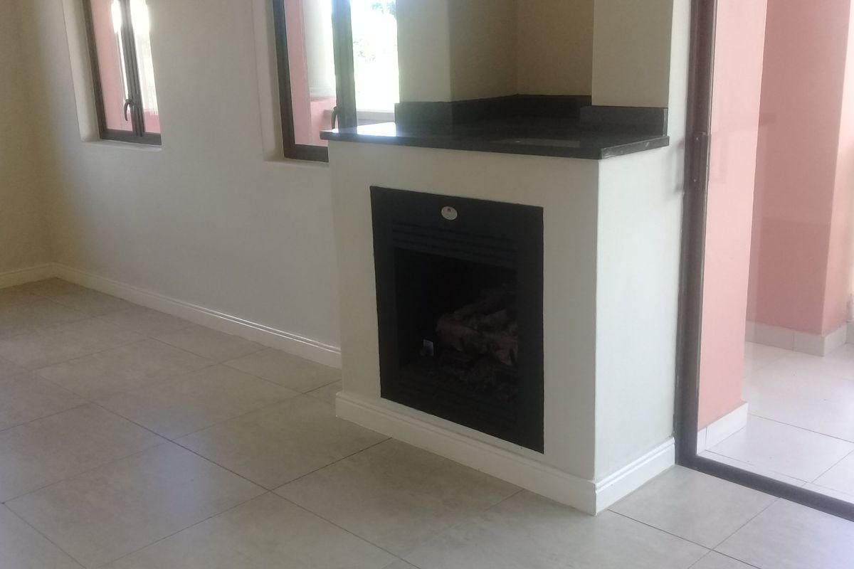 A bright, empty living room featuring a modern built-in fireplace with a stone hearth, neutral tiled flooring, and direct access to an outdoor balcony.