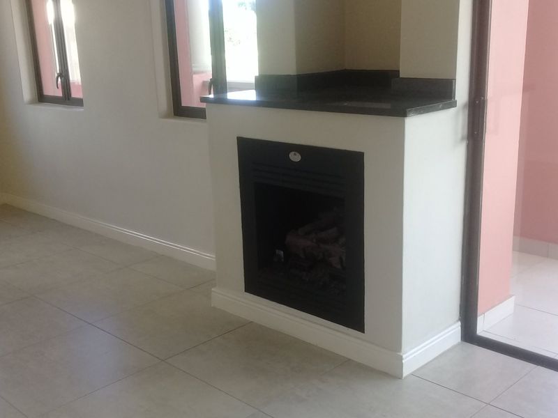 A bright, empty living room featuring a modern built-in fireplace with a stone hearth, neutral tiled flooring, and direct access to an outdoor balcony.
