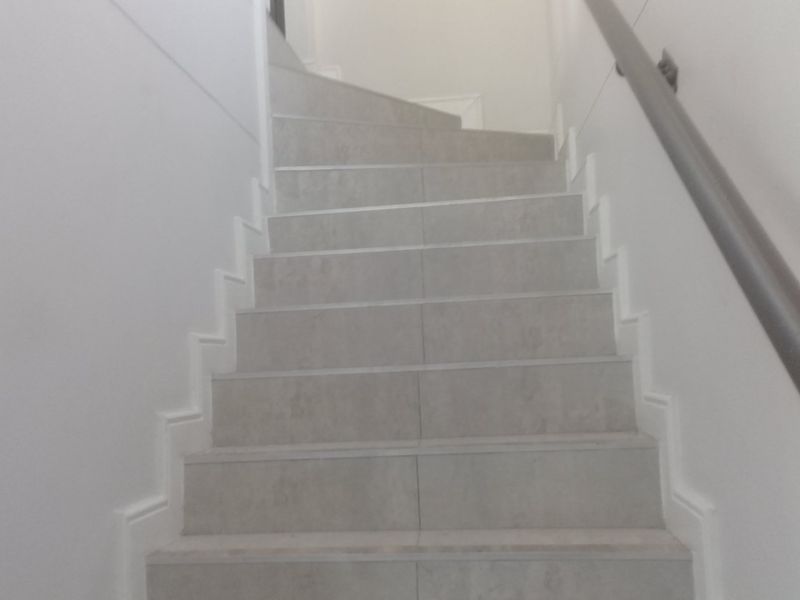A clean, modern staircase featuring neutral-toned tiled steps and a simple handrail, providing a bright and minimalist transition between levels.
