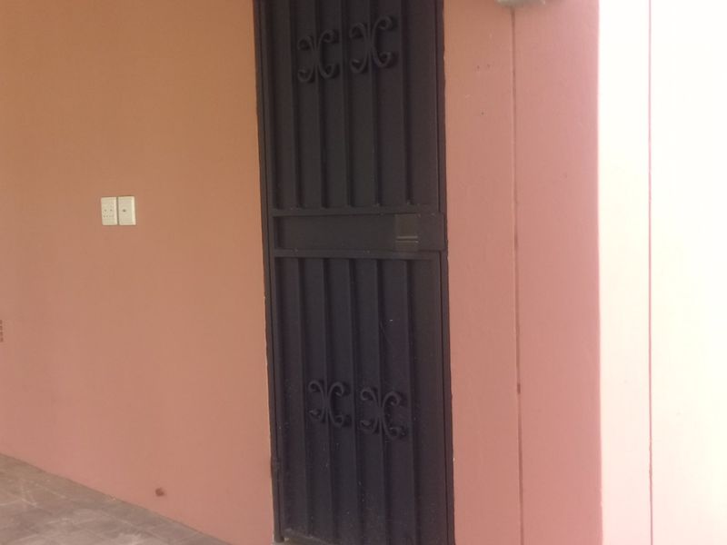 A covered exterior entrance area featuring a black metal security gate and tiled flooring.