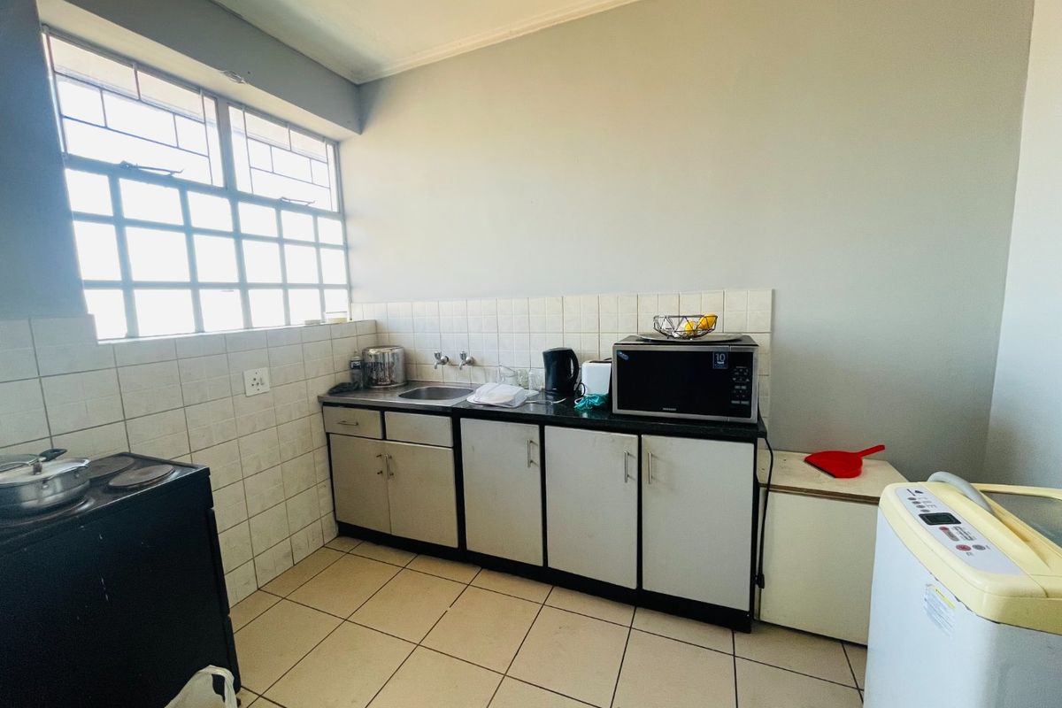 A functional kitchen area featuring tiled splashbacks, built-in cabinetry, and a stainless steel sink, offering potential for modernization and aesthetic updates.