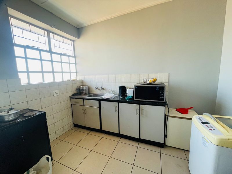 A functional kitchen area featuring tiled splashbacks, built-in cabinetry, and a stainless steel sink, offering potential for modernization and aesthetic updates.