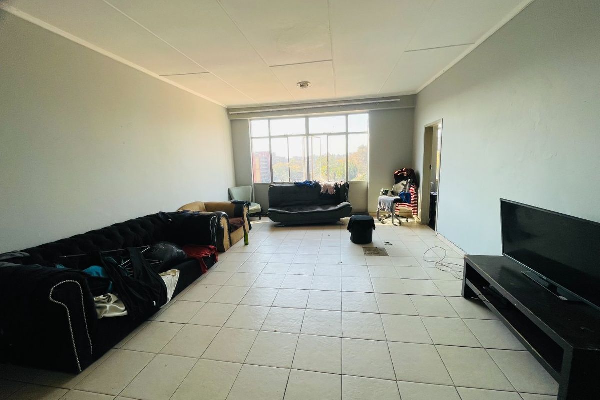 Spacious living area featuring large windows for natural light and tiled flooring throughout, offering a blank canvas for potential renovation and interior design updates.