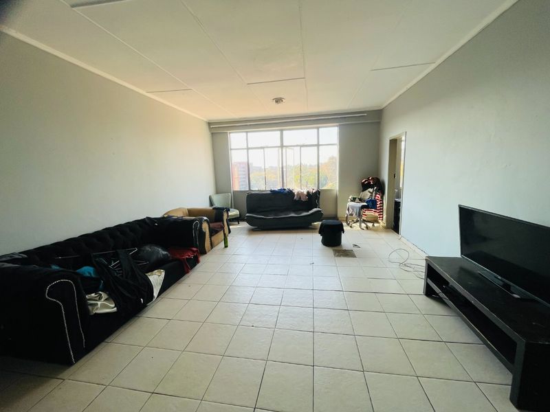 Spacious living area featuring large windows for natural light and tiled flooring throughout, offering a blank canvas for potential renovation and interior design updates.