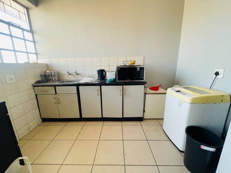 A functional laundry area featuring built-in cabinetry, a stainless steel sink, tiled backsplash, and tiled flooring with space for laundry appliances.