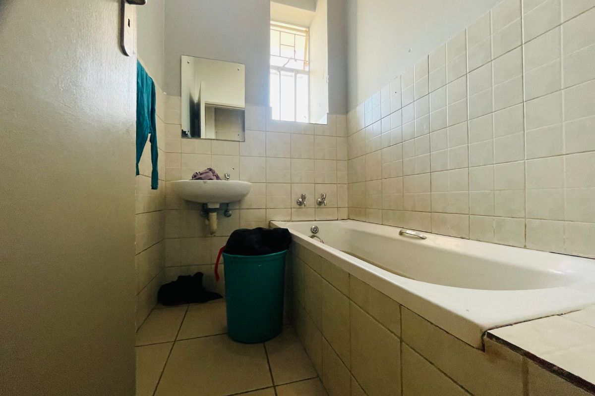 A functional bathroom featuring a bathtub, wall-mounted basin, and tiled finishes, offering potential for modernization and cosmetic updates.