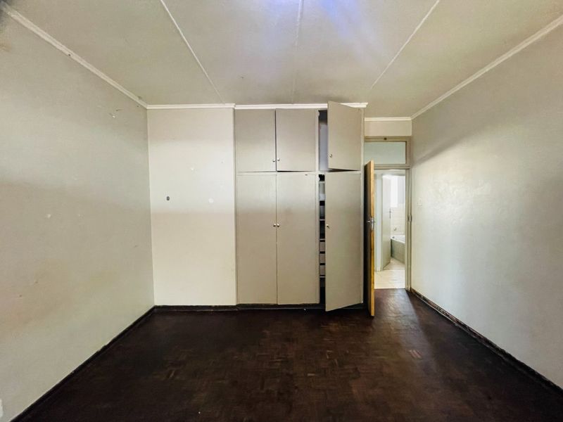 An empty bedroom featuring original parquet flooring and built-in storage cupboards, with direct access to an adjacent bathroom.