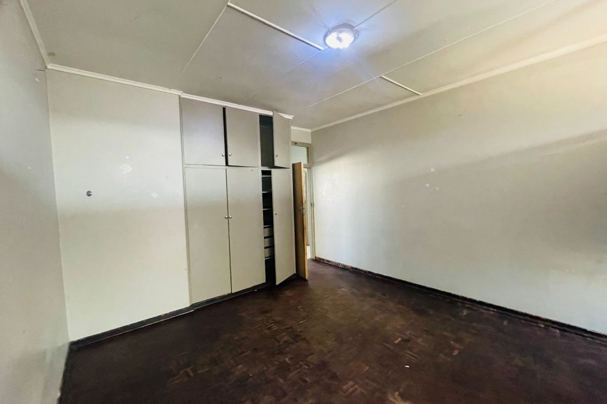 An empty bedroom featuring original parquet flooring, built-in cupboards, and a standard ceiling, offering a blank canvas for renovation and modernization.