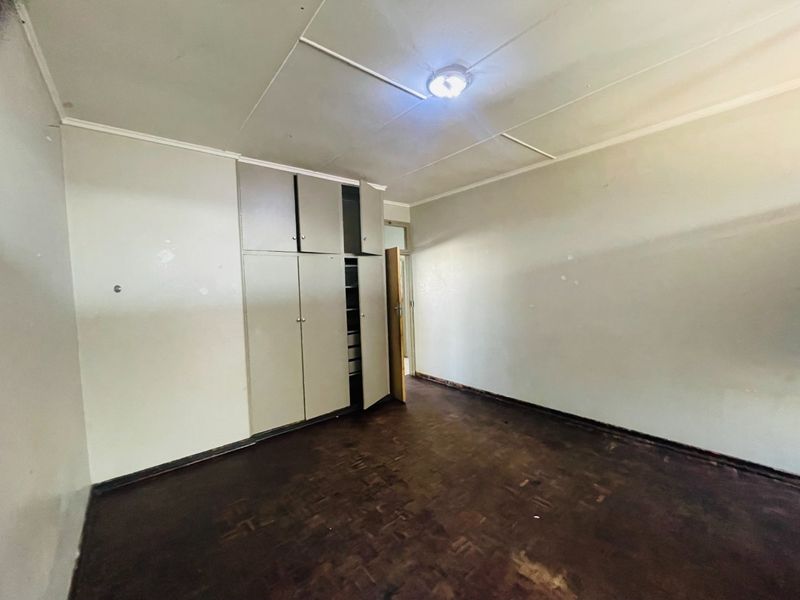 An empty bedroom featuring original parquet flooring, built-in cupboards, and a standard ceiling, offering a blank canvas for renovation and modernization.