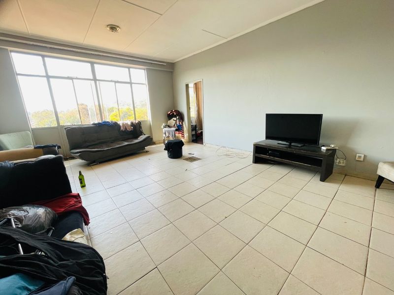 Spacious living area featuring large windows for natural light and tiled flooring, requiring cosmetic updates to enhance its appeal.