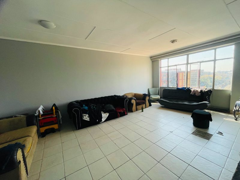 Spacious living area featuring large windows for natural light and tiled flooring, requiring some maintenance to ceiling and floor finishes.