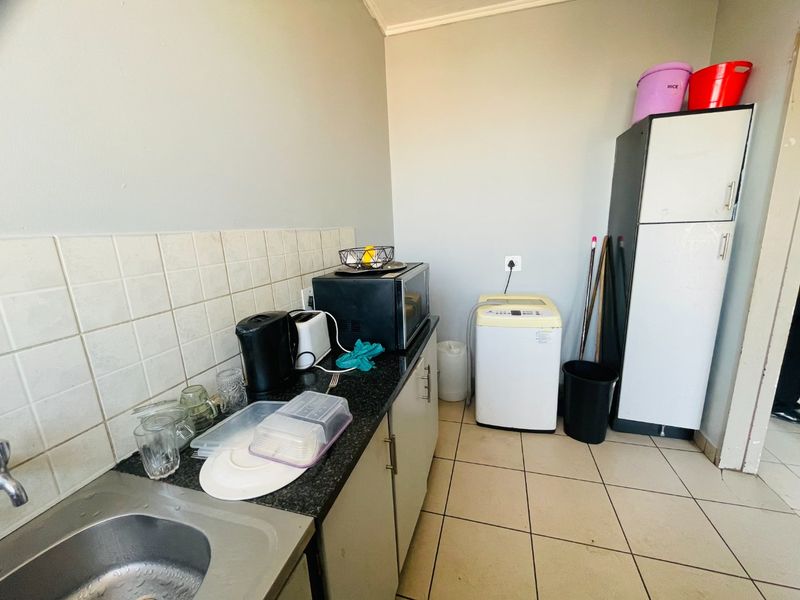 A functional laundry area featuring built-in cabinetry, a granite countertop, a stainless steel sink, and tiled flooring.