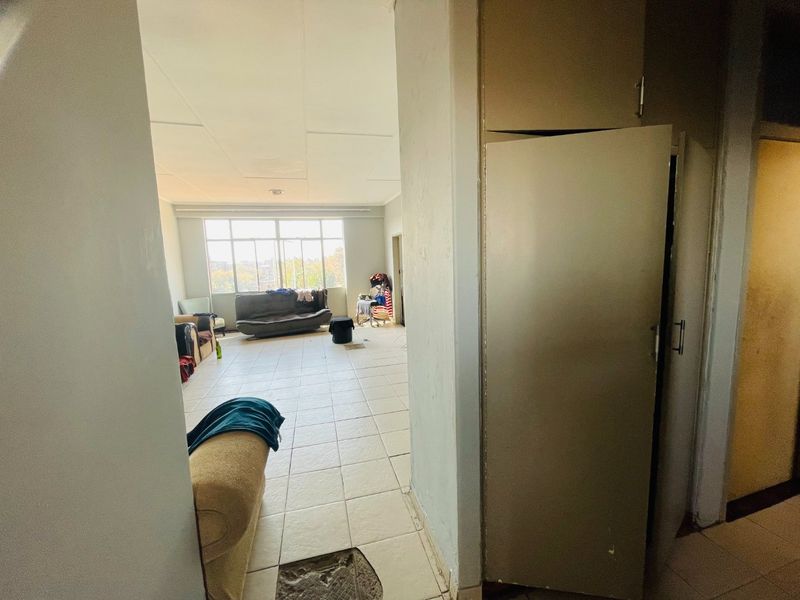 A spacious living area featuring tiled flooring, a large window providing natural light, and a built-in storage cupboard.