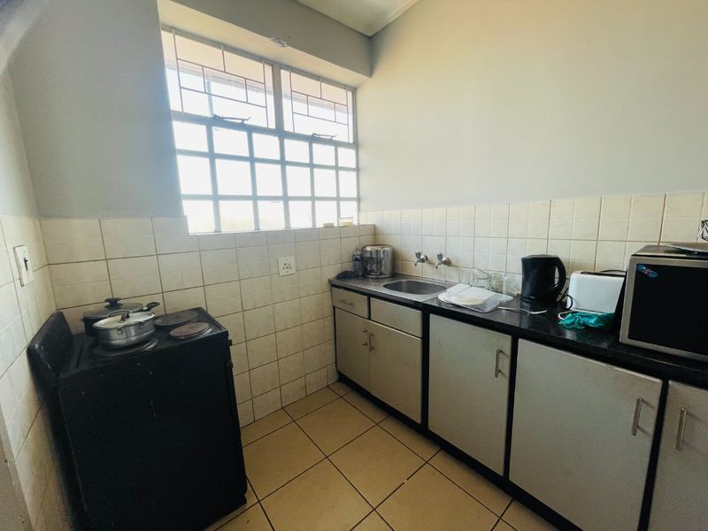 A functional kitchen featuring tiled backsplash, stainless steel sink, and laminate cabinetry with tiled flooring and security window bars.