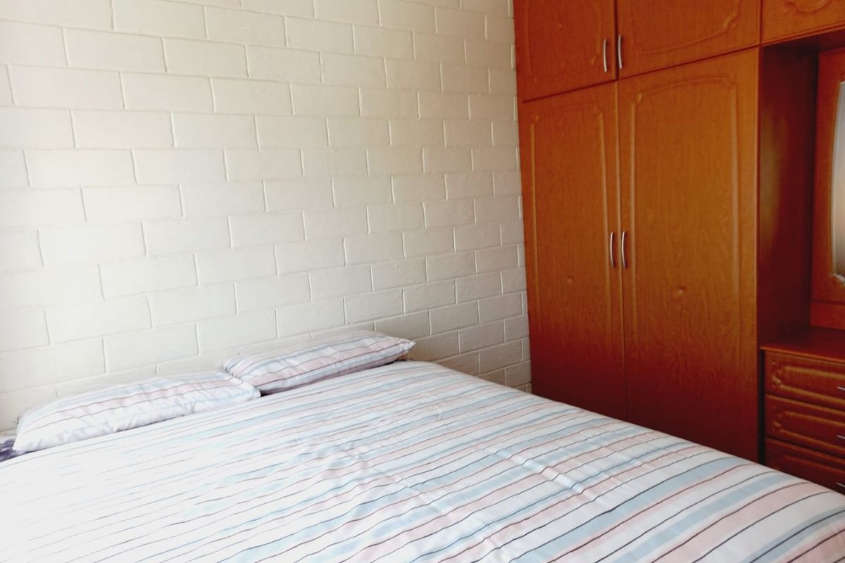 A bedroom featuring a built-in wooden wardrobe and a painted exposed brick wall.