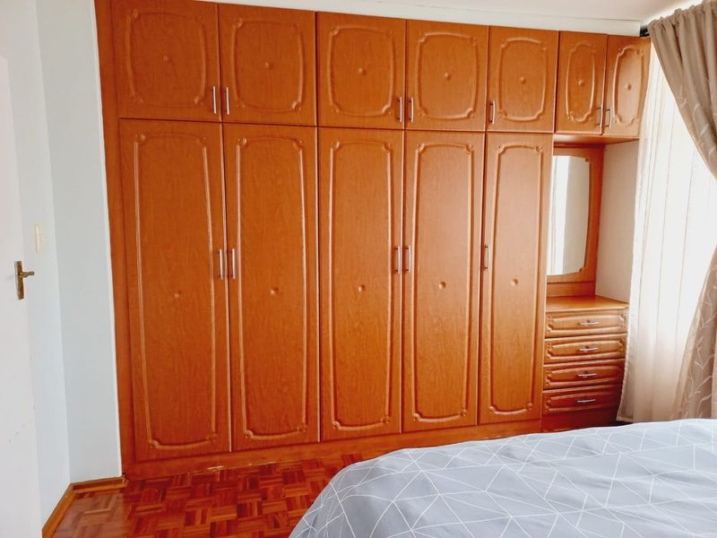 Bedroom featuring extensive floor-to-ceiling wooden built-in cupboards with integrated vanity and drawers, complemented by classic parquet flooring.