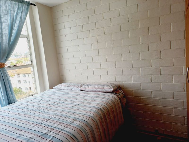 A bedroom featuring a painted brick accent wall and a large window providing natural light and an urban view.