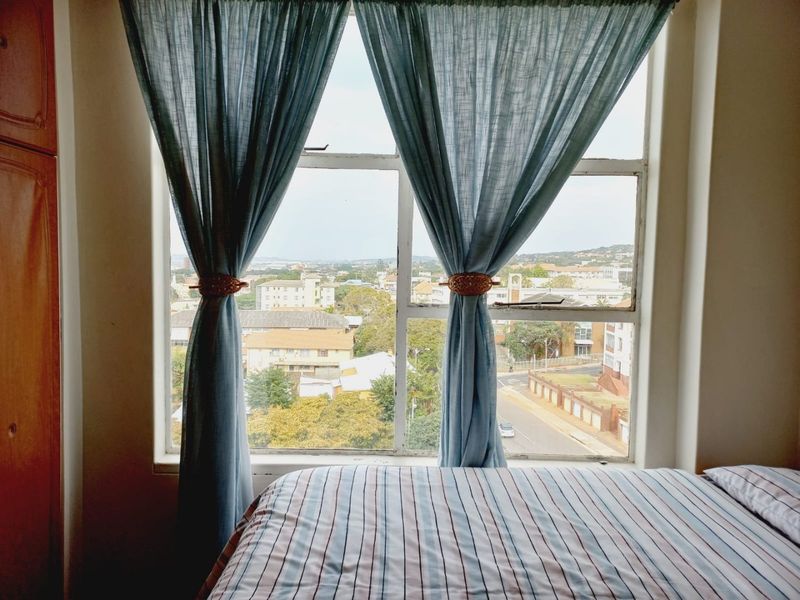 A bedroom featuring a built-in wardrobe and a large window offering an elevated urban view.