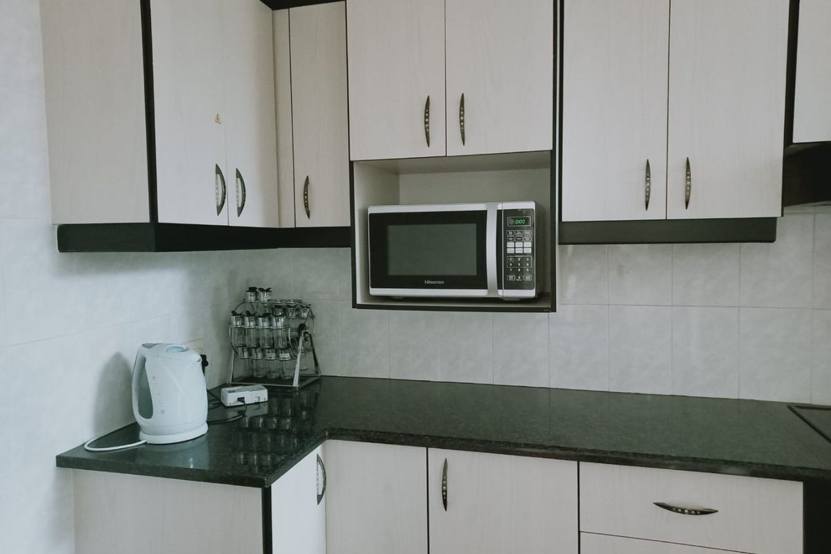 A functional kitchen featuring light-toned cabinetry with dark trim, granite countertops, and a built-in microwave space.