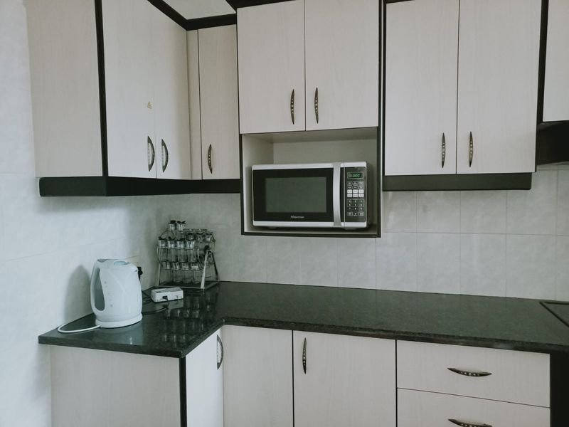 A functional kitchen featuring light-toned cabinetry with dark trim, granite countertops, and a built-in microwave space.