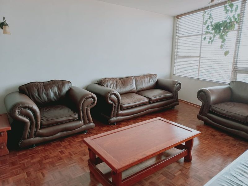 A living room featuring classic parquet flooring and large windows fitted with venetian blinds, offering a neutral space ready for modern updates.