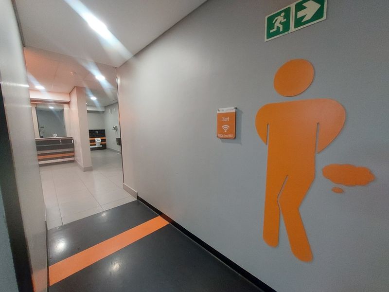 A clean, modern commercial hallway featuring tiled flooring, recessed lighting, and clear directional signage leading toward the restroom facilities.