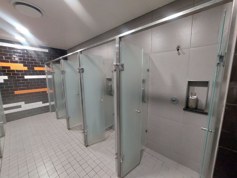 A modern commercial bathroom facility featuring multiple private stalls with frosted glass partitions, tiled surfaces, and recessed wall storage niches.