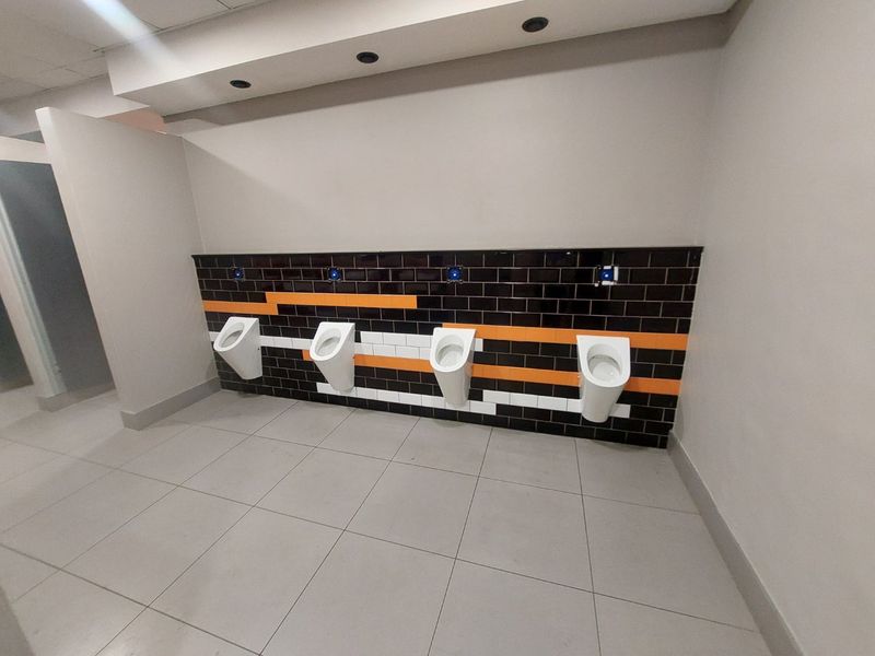A clean, modern commercial restroom facility featuring a row of four wall-mounted urinals with decorative black, white, and orange tiled wall accents.
