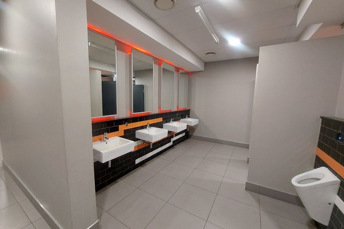 Modern commercial restroom featuring multiple wall-mounted washbasins, tiled splashbacks, integrated LED mirror lighting, and a clean, functional layout with ceramic flooring.