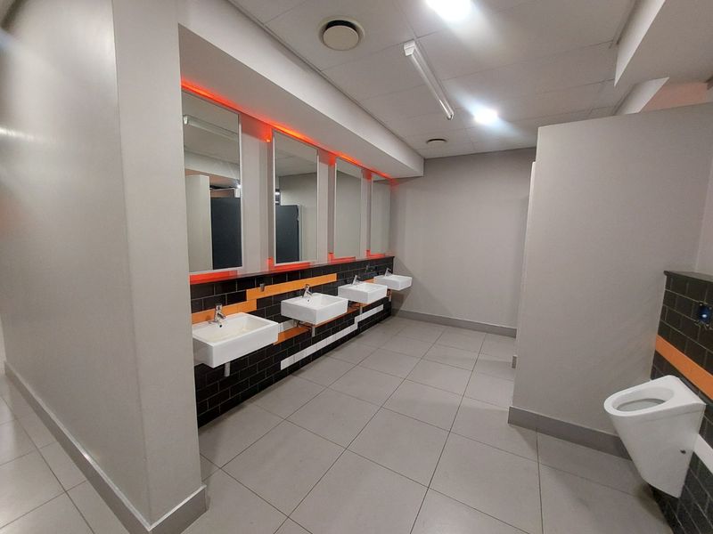 Modern commercial restroom featuring multiple wall-mounted washbasins, tiled splashbacks, integrated LED mirror lighting, and a clean, functional layout with ceramic flooring.
