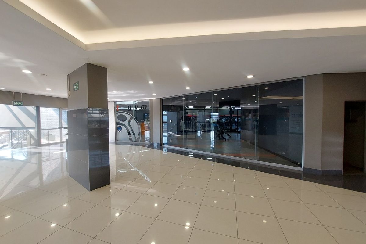 A modern commercial gym space featuring polished tile flooring, recessed ceiling lighting, and a large glass storefront facade.