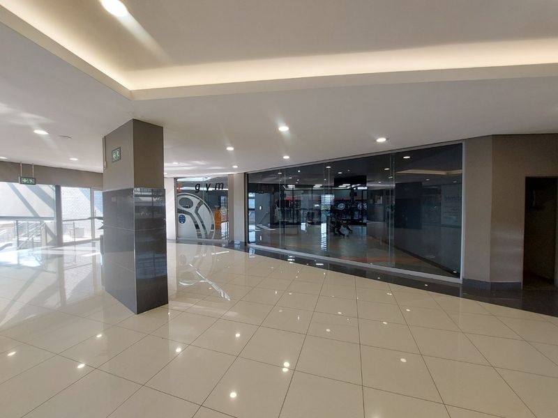 A modern commercial gym space featuring polished tile flooring, recessed ceiling lighting, and a large glass storefront facade.
