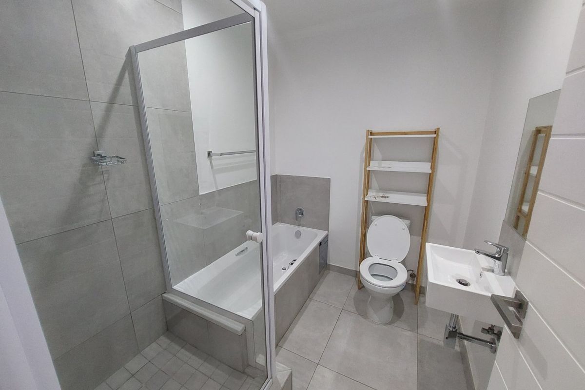 Modern bathroom featuring a glass-enclosed shower, a separate bathtub, a wall-mounted basin, and neutral grey floor-to-ceiling tiling.