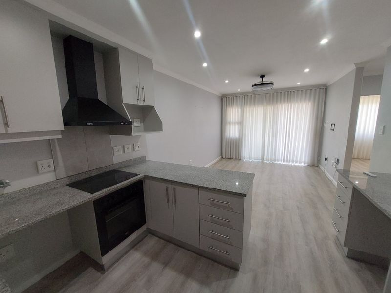 Modern open-plan kitchen and living area featuring granite countertops, built-in appliances, recessed lighting, and light laminate flooring in a clean, vacant space.